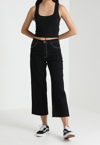 Czarny krótki top na ramiączkach, czarne dżinsy z wysokim stanem i szerokimi nogawkami ze kontrastowym przeszyciem, zestawione z czarno-białymi sneakersami.