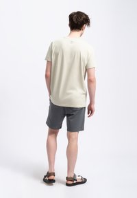 Lichtbeige t-shirt met korte mouwen, gecombineerd met donkere grijze shorts. De shorts hebben een gladde textuur en subtiele stiksel details.