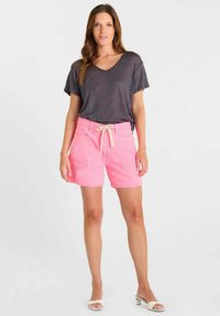 Roze katoenen korte broek met een trekkoord in de taille en twee voorzakken, gecombineerd met een donkergrijs T-shirt met korte mouwen. Gladde textuur.