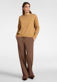 Maglione a maglia color senape con colletto rotondo e polsini decorati, abbinato a pantaloni larghi marroni a vita alta. Texture liscia.