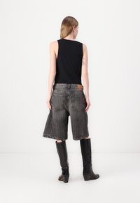 Svart ermeløs topp kombinert med grå denimshorts, med løs passform, slitt kant og to baklommer. Knelengde svarte støvletter fullfører utseendet.