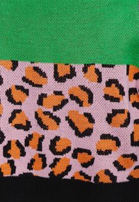 Pull en maille avec des rayures horizontales vertes et roses, avec un motif léopard en orange et noir en bas. Ourlet côtelé noir.