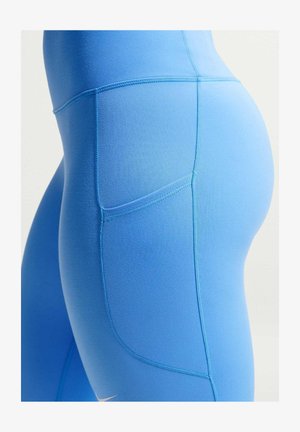 Primer plano de leggings azul claro con un bolsillo lateral y costuras visibles en la cadera y el muslo de una persona.