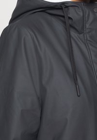 Svart vattentät jacka med huva, som har en slät yta, justerbara dragsko och tryckknappsstängningar.