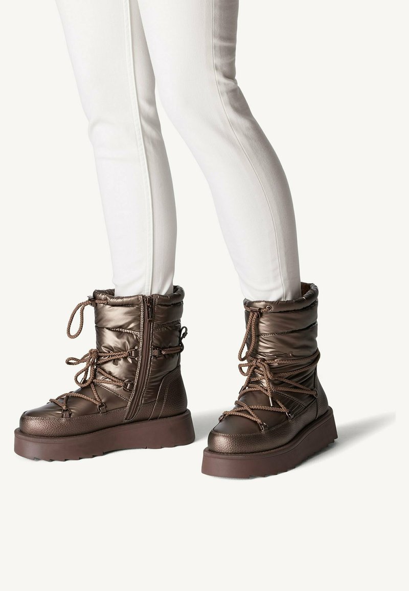 Botas de tobillo aisladas de color marrón con una textura lisa y brillante, que cuentan con un diseño de cordones, un cierre lateral con cremallera y una suela gruesa.
