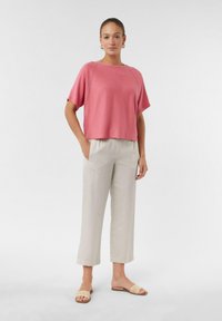 Rosa Kurzarmoberteil mit lockerem Schnitt, kombiniert mit hellbeigen, cropped Hosen. Das Outfit zeichnet sich durch ein schlichtes Design und eine angenehme Textur aus.