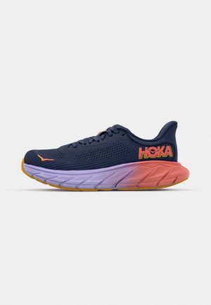 Men's running shoes in navy mesh with perforations. Thick gradient sole transitions from lilac to coral with orange accents and logo.