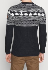 Gebreide trui in donker marineblauw met een geribbelde textuur, featuring een witte patroon op de schouder en een leren merkpatch op de linkerschouder.
