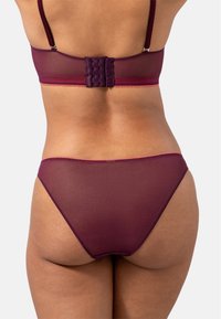 Vibrantti burgundin värinen alusvaatesetti, jossa on läpinäkyvä kangas, säädettävät olkaimet ja viisi hakasta suljettava rintaliivi. Tanga-tyyliset alushousut.