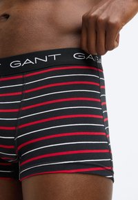 Fekete csíkos boxeralsó vízszintes piros és fehér csíkokkal, fekete elasztikus derékpánttal, amelyen a "GANT" logó látható, valamint puha anyagminőséggel.