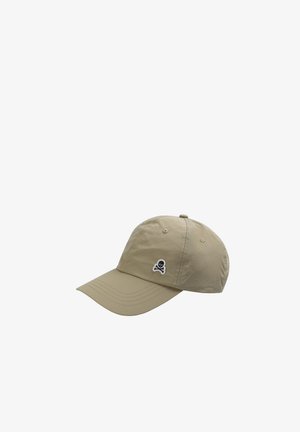 Gorra de béisbol beige con visera curva y pequeño emblema de calavera y huesos cruzados en blanco y negro en el panel frontal izquierdo.