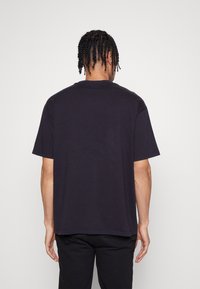 Svart kortärmad T-shirt i bomull med rundad halsringning, som har en avslappnad passform och mjuk textur. Bakifrån syns inga logotyper eller mönster.