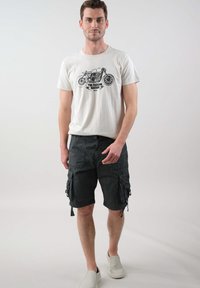 Witte t-shirt met motorfietsafbeelding, gecombineerd met zwarte cargoshorts met zijzakken en trekkoorden, afgerond met lichte instappers.