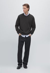 Czarny sweter z dzianiny nałożony na jasnoniebieską koszulę z kołnierzykiem, w połączeniu z ciemnoniebieskimi dżinsami i czarnymi butami. Prosty, casualowy design z luźnym krojem.