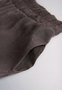 Pantalon en lin gris foncé avec une taille élastique et une poche latérale, présenté sur une surface blanche.