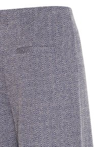 Gros plan sur un tissu à chevrons bleu et blanc avec une petite poche passepoilée à l’arrière d’un vêtement, montrant une texture tissée détaillée.