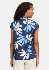 Camicia in tessuto navy con design floreale blu e crema, maniche corte e colletto arricciato, dal taglio morbido e con spacchi laterali.