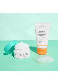 White jar with a turquoise lid containing cream; white tube with orange accents holds jelly cleanser. Background in soft mint green.