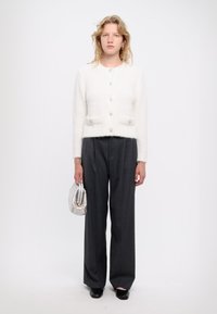 Weißer, flauschiger Cardigan mit Rundhalsausschnitt und fünf dekorativen Knöpfen, kombiniert mit hoch taillierten, weiten grauen Hosen und einer silbernen Clutch.