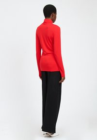 Rotes Langarm-Turtleneck-Oberteil mit figurbetonter Silhouette. Kombiniert mit lockeren schwarzen weiten Hosen und weißen High-Heels.