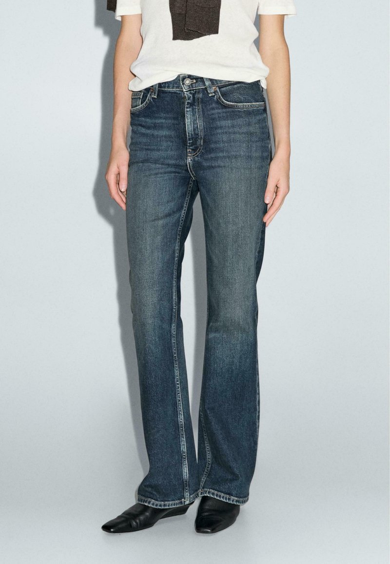 Jeans in denim blu scuro con taglio dritto, dotati di cinque tasche e dettagli di cucitura discreti lungo le cuciture.