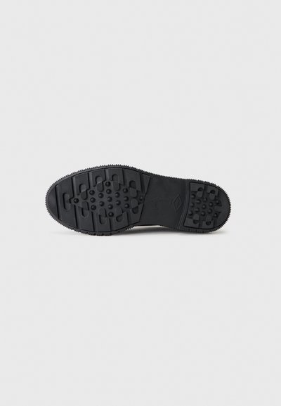 Μαύρη σόλα παπουτσιού με σχέδιο πέλματος που περιλαμβάνει ορθογώνιες αυλακώσεις και κυκλικά καρφιά σε ανοιχτό γκρι φόντο.