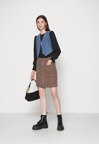 Veste en denim au design court, chemise noire à manches longues, jupe à carreaux marron avec fermeture éclair à l'avant, bottes à talons noires et sac à main.