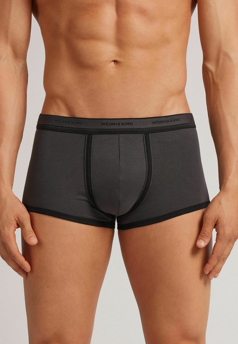 Šedé boxer šortky vyrobené z měkkého materiálu, s černým pasem s logem, přizpůsobený střih a hladká textura.