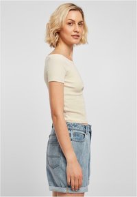 Ljus beige, figursydd topp med kort ärm, kombinerad med högmidjade ljusblå denimshorts som har upprullade ärmslut och bakfickor.