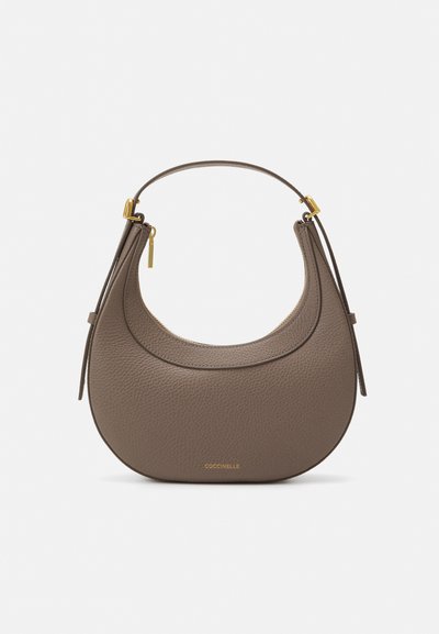 Sac à main en cuir brun avec texture granulée, de forme incurvée, accents en métal doré et une courte poignée. Fermeture éclair avec un logo visible à la base.