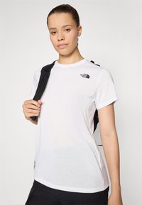 T-shirt bianco a maniche corte realizzato in tessuto morbido, con un piccolo logo nero sulla parte superiore sinistra e un collo rotondo.
