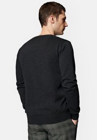 Ciemnoszary sweter z długimi rękawami, okrągłym dekoltem, ściągaczami przy rękawach i dolnym brzegu, uszyty z miękkiej tkaniny, noszony na szkockich spodniach.