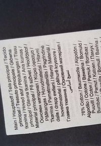 Étiquette d'entretien en tissu de coton avec plusieurs langues, affichant du texte noir sur un fond clair, comprenant des détails de composition du matériau.