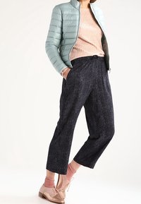 Jasnoniebieska kurtka puchowa, różowy sweter w prążki, ciemne teksturowane spodnie o kroju 7/8, różowe skarpetki oraz stylowe beżowe buty ze sznurowadłami.