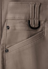 Tessuto beige con una texture liscia e cuciture visibili; presenta un anello a D in metallo nero e due bottoni a pressione neri sulle tasche.