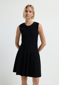 Abito senza maniche nero con corpetto aderente e gonna ampia, caratterizzato da cuciture verticali e scollo tondo. Tessuto di trama liscia.
