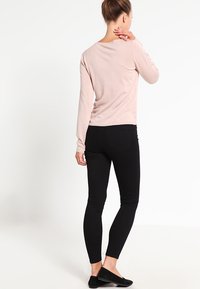 Rosa tröja med långa ärmar, mjuk textur och rund halsringning, kombinerad med svarta tajta jeans och svarta platta skor, sedd bakifrån.
