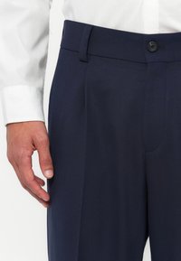 Pantalons de costume bleu marine avec une coupe droite, fermeture à bouton et poches latérales. Fabriqués en tissu texturé, ils offrent une coupe ajustée.