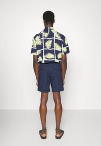 Lyhythihainen, tummansininen kukkapaidoissa, joissa on vaaleanvihreitä palmun kuvioita, yhdistetty tummansiniin shortseihin. Ominaisuutena rento istuvuus ja teksturoitu kangas.