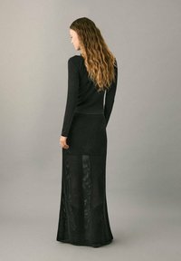 Top negro de manga larga combinado con una falda maxi negra de punto transparente con estampado de estrellas, que exhibe un diseño ajustado.