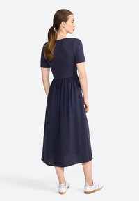Robe bleu marine, longueur genou, avec un corsage ajusté en maille côtelée, des manches courtes et une jupe fluide et texturée. Portée avec des baskets blanches.