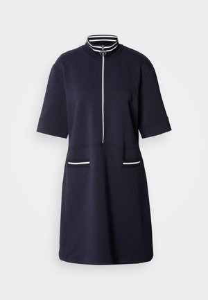 Marineblauwe jurk met korte mouwen, hoge kraag en een rits aan de voorkant. Kenmerkt zich door witte gestreepte accenten op de kraag en twee voepockets.