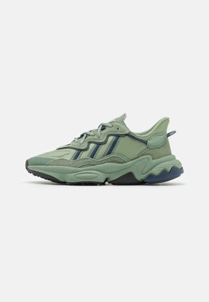 Baskets de sport vertes avec une tige texturée, un design de matériaux superposés, des accents bleu foncé et une semelle épaisse. Elles sont dotées de lacets et d'une languette.