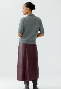 Grijze gebreide polo met korte mouwen, gedragen met een bordeaux faux leren maxi rok, gekenmerkt door diagonale panelen en een gladde afwerking.