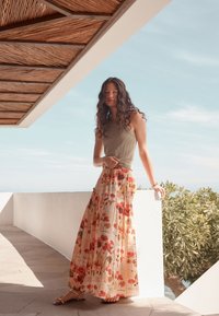 Langer Blumennrock in Creme mit roten und gelben Mustern, kombiniert mit einem eng anliegenden grauen Tanktop. Das Outfit besticht durch ein fließendes Design und eine weiche Textur.