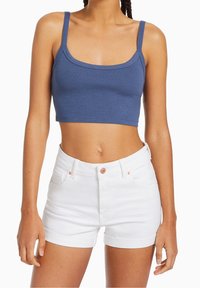 Blå kort topp i mjukt material med justerbara band, parat med vita denimshorts med knapp och uppvikta fållar.