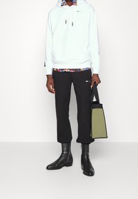 White hoodie with drawstring, black sweatpants, black ankle boots, and an olive green bag. Layered floral shirt under the hoodie.