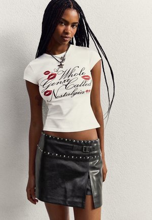 Witte fitted t-shirt met een grafisch ontwerp van rode lippen en scripttekst, gecombineerd met een zwart neplederen minirok met studs en een zijsplit.