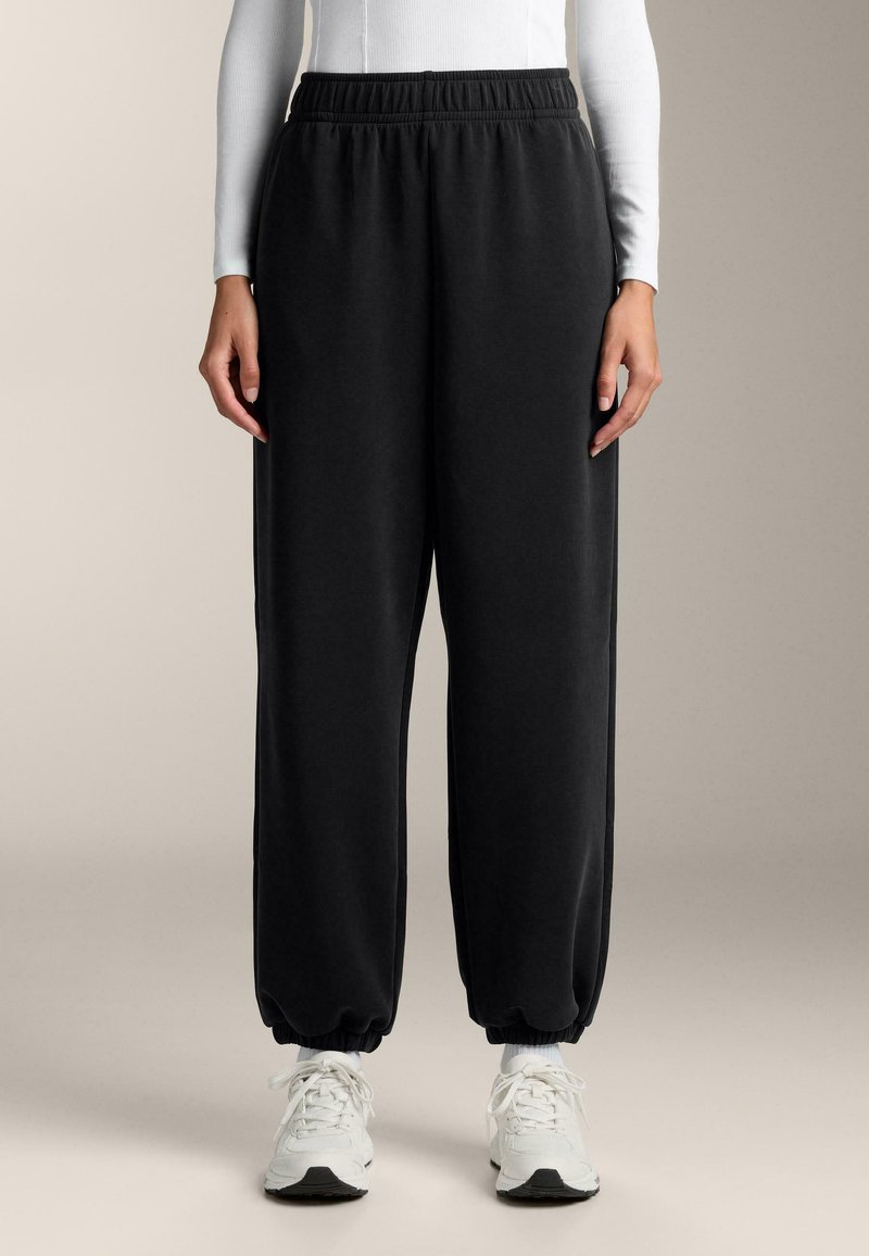 Čierne tepláky vyrobené z mäkkej textílie, s elastickým pásom a manžetami, uvoľneného strihu a bočnými vreckami.