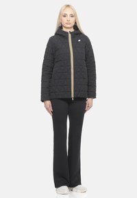 Schwarze gesteppte Jacke mit Kapuze, hervorgehoben durch einen gelben Reißverschluss, mit einem geometrischen Muster und langen schwarzen Hosen.